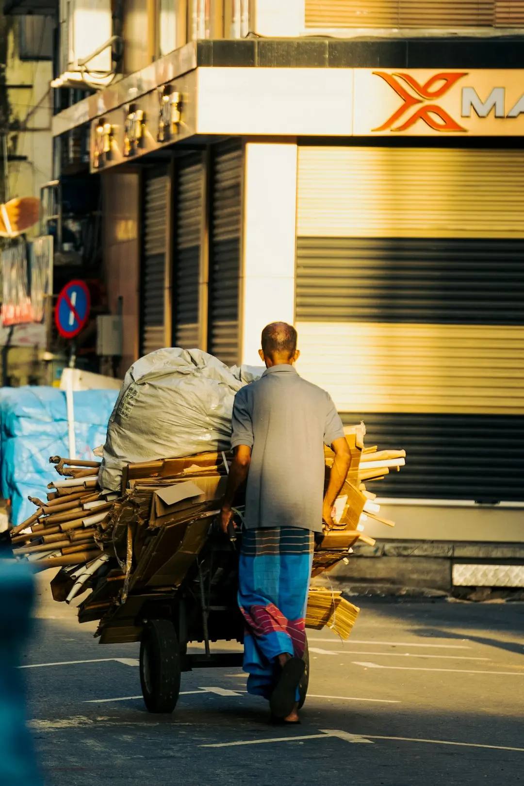 A person pushing a cart loaded with cardboard and plastic on a city street